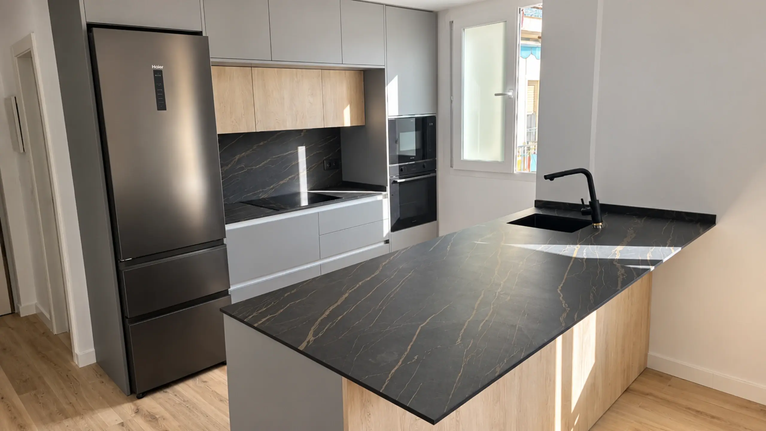 Cocina con península de encimera negra veteada y fregadero, frigorífico de acero y frontal oscuro