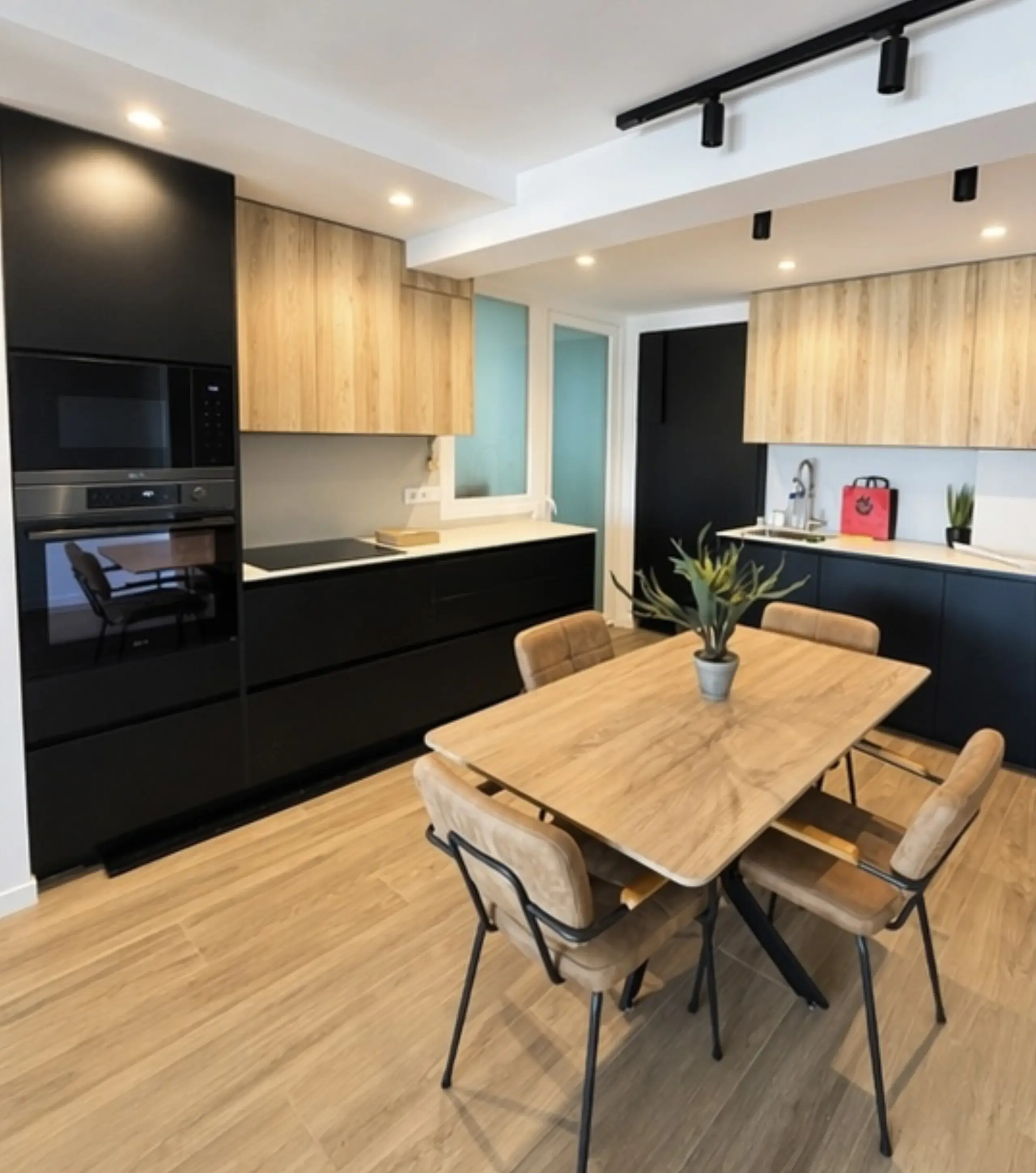 Cocina en negro y madera con mesa de comedor de madera en el centro y focos en carril negro en el techo