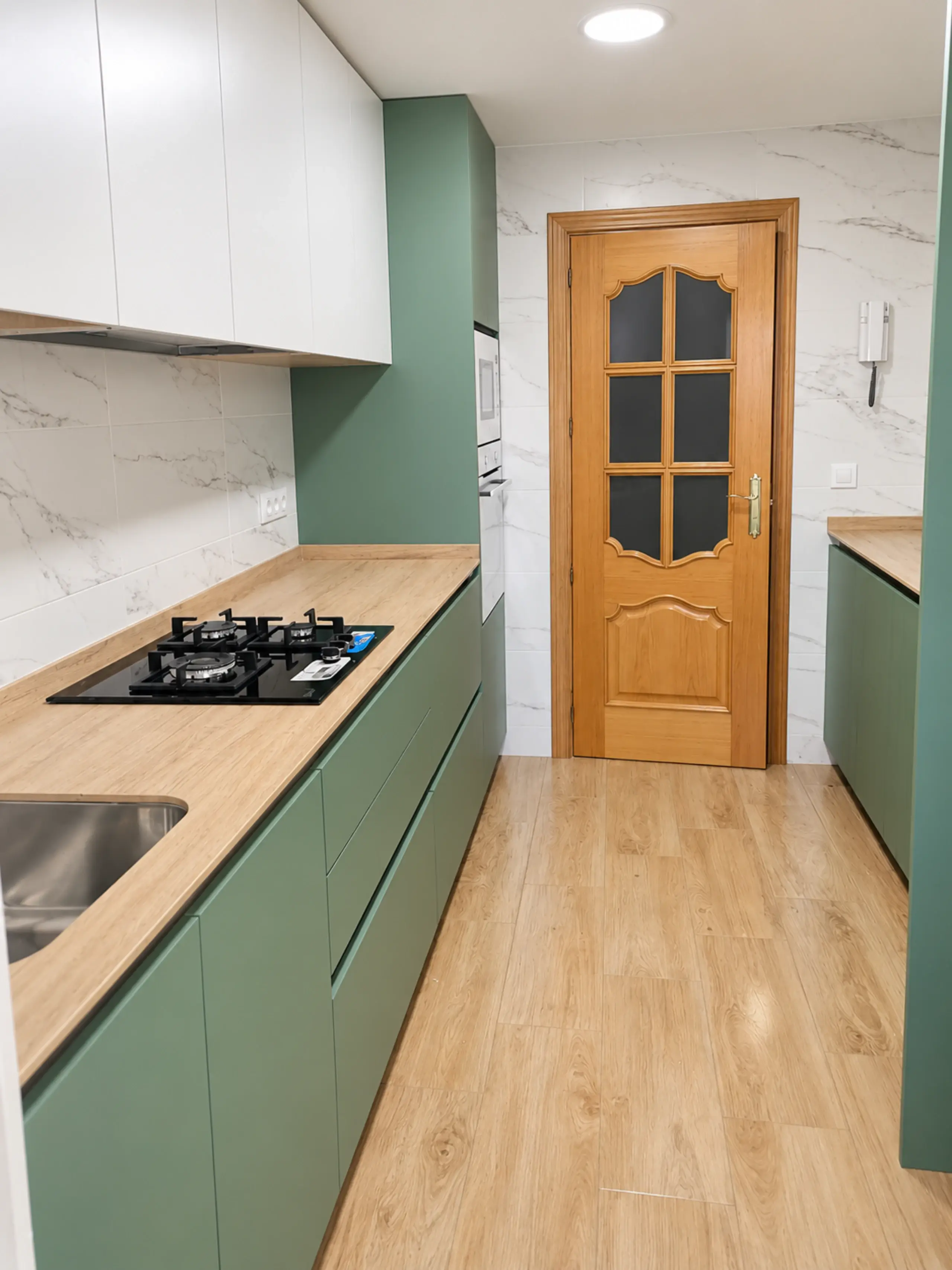 Cocina en paralelo en verde y madera vista hacia la puerta de madera del fondo
