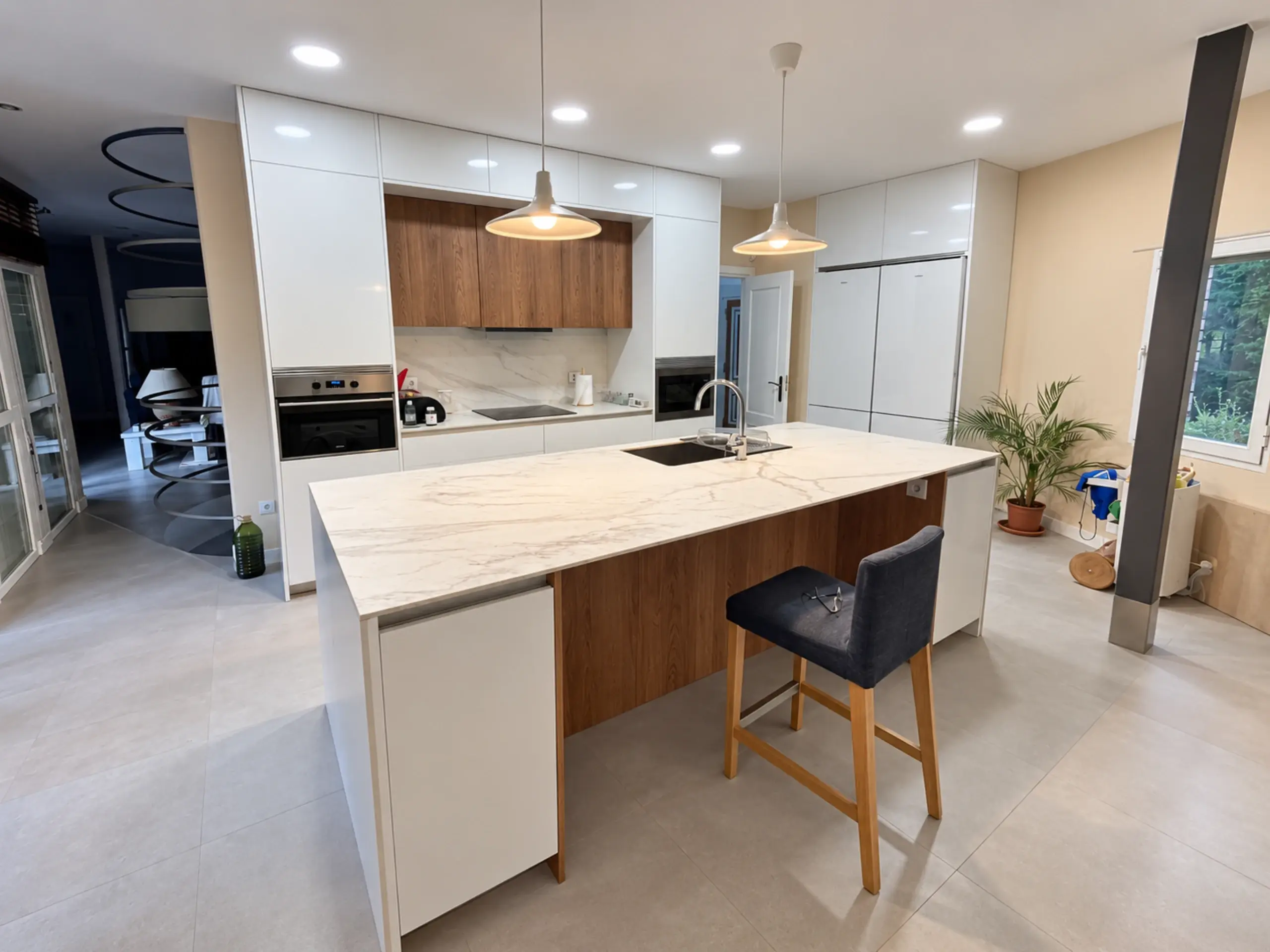 Isla blanca con taburetes de madera y muebles altos de madera al fondo