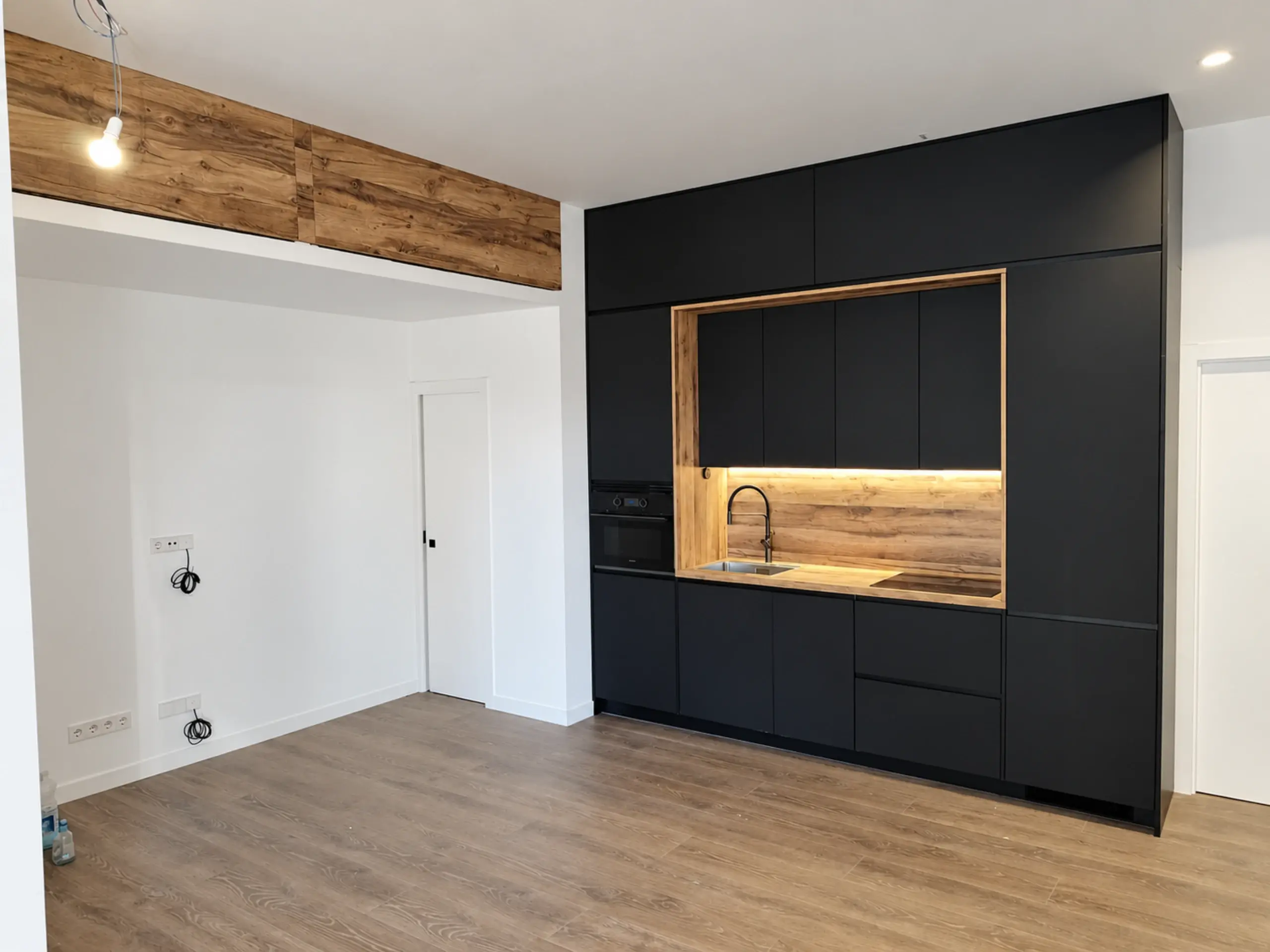 Cocina puente negra en un salón abierto con viga de madera en el techo
