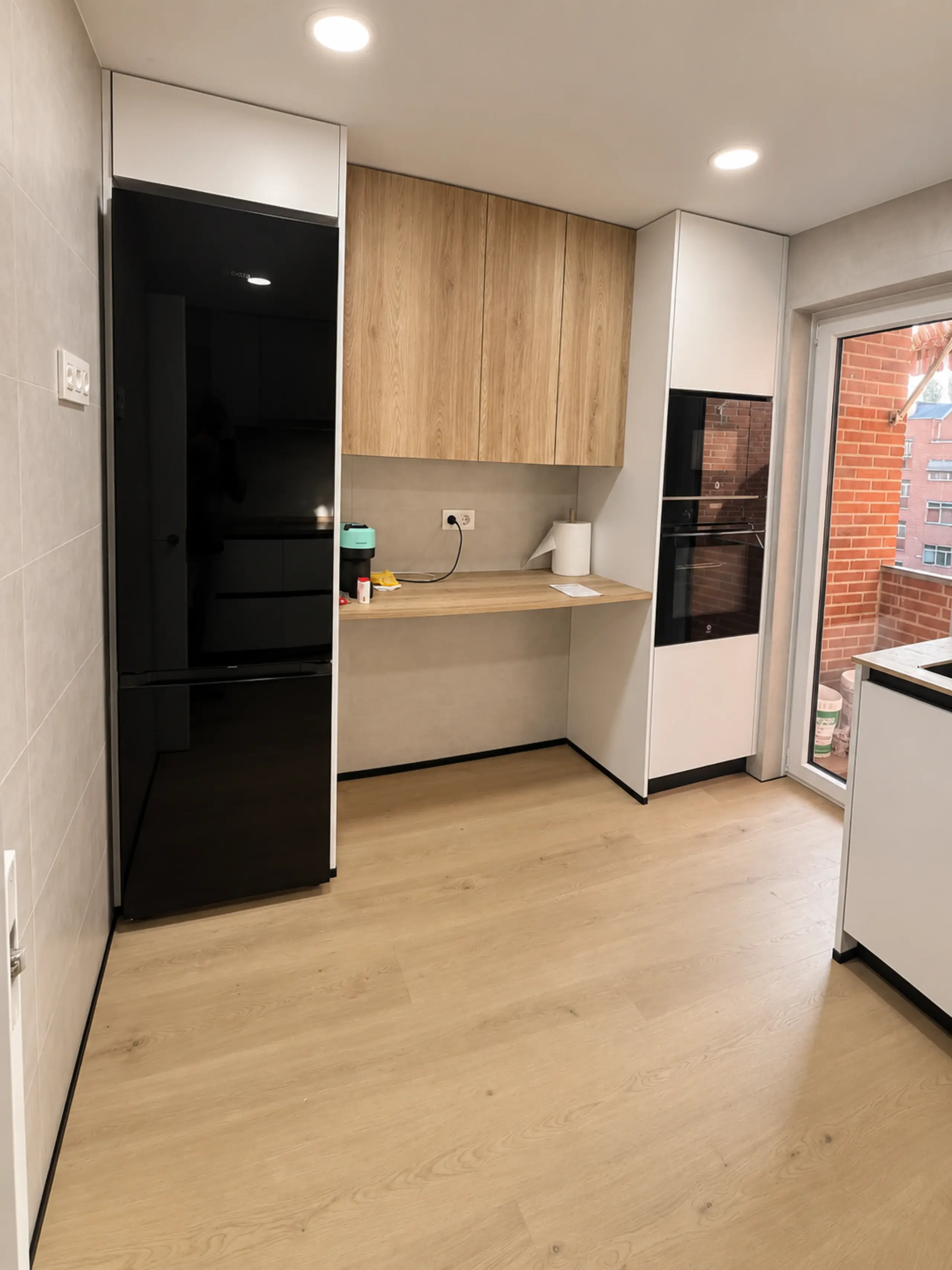 Frigorífico negro, muebles altos de madera y zona de escritorio en la cocina en L
